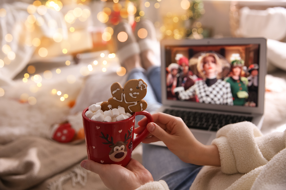 Woman with sweet drink watching The Witches movie on laptop at home, closeup. Cozy winter holidays atmosphere