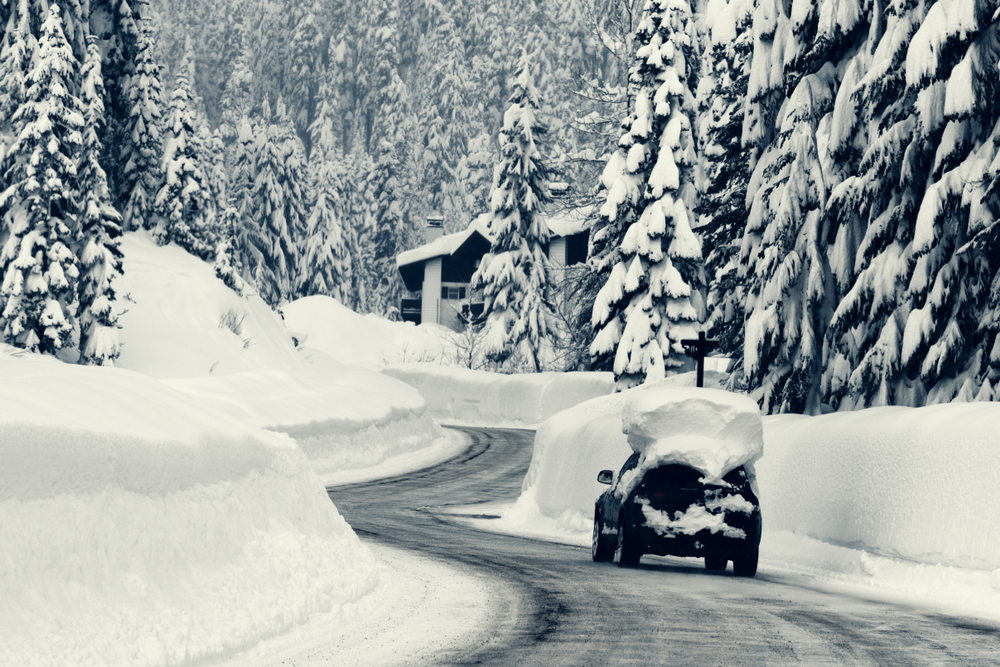 Freshly plowed mountain road with deep snow on sides and on top of automobile.