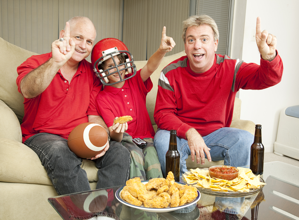 A little boy watching the super bowl with his father and uncle.