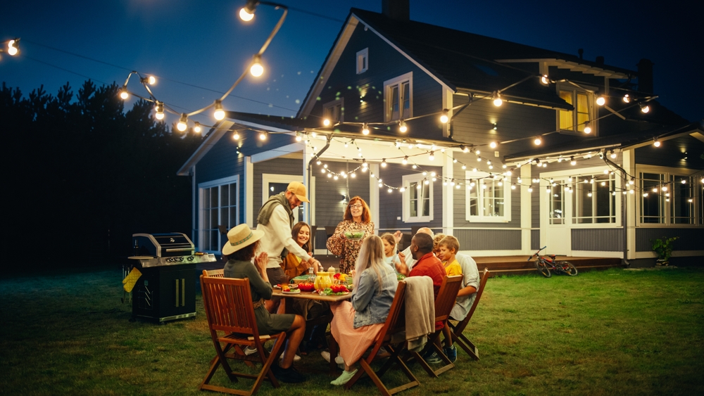 Group of Multiethnic Diverse People Having Fun, Sharing Stories with Each Other and Eating at Outdoors Dinner Party. Family and Friends Gathered Outside Their Home on a Warm Summer Evening.