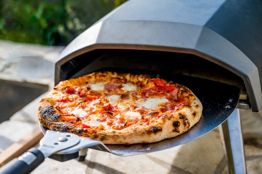 Making homemade pizza in portable high temperature gas oven. Delicious pizza is baking in gas oven furnace for home made Neapolitan pizza. Special gas fueled pizza oven for picnic or party.