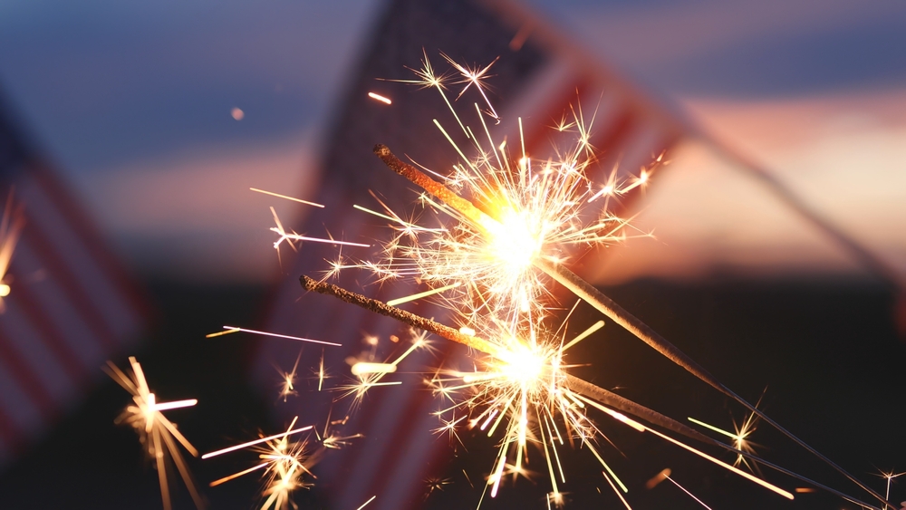 Fireworks sparklers fourth of July, Happy USA Independence Day Holiday, Celebration. Hands Holding Sparklers Fireworks with USA American Flag at sunset outdoor background. Concept 4th of July, Freedom
