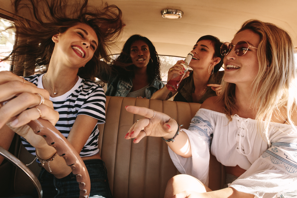 Group of happy young women laughing and enjoying in car during a road trip to vacation. Girls having fun on road trip.
