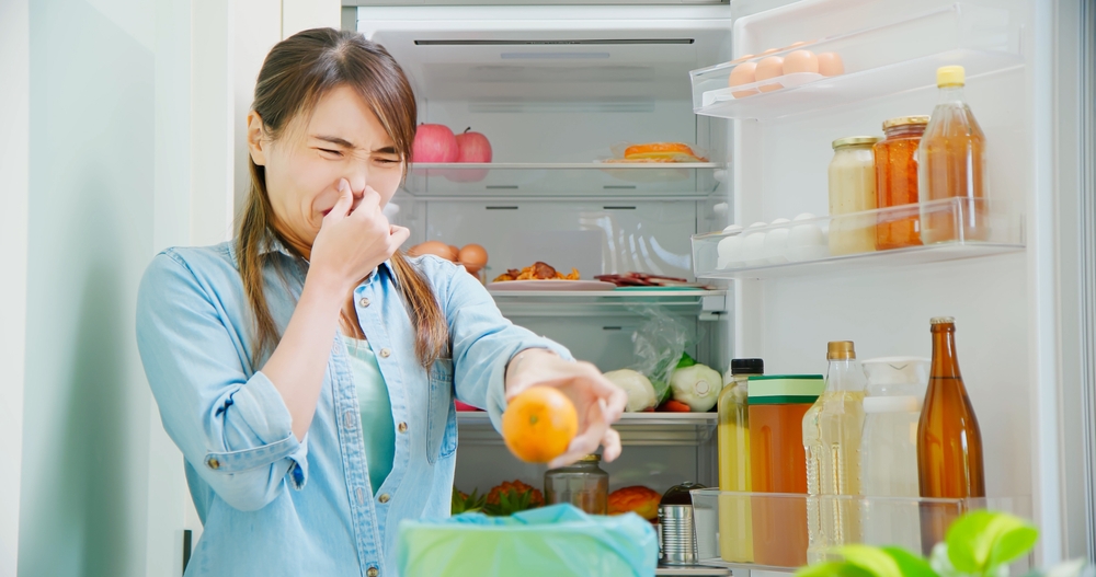 asian woman is cleaning refrigerator and pouring food waste which smell bad into kitchen bucket at home
